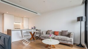 A modern living room with a grey sofa, a coffee table, and a dining area with chairs. - High-level 1 Bedroom Apartment in Fortitude Valley (Fortitude Valley)