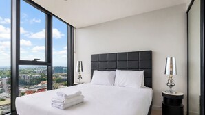 A hotel room with a large bed, two bedside lamps, a view of the city, and a cityscape visible through the window. - High-level 1 Bedroom Apartment in Fortitude Valley (Fortitude Valley)