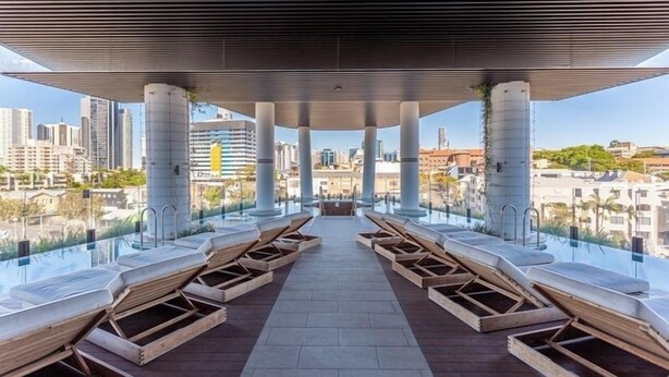 A rooftop terrace with a pool, lounge chairs, and a city view. - High-level 1 Bedroom Apartment in Fortitude Valley (Fortitude Valley)