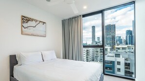 A modern hotel room with a large bed, a city view, and a painting on the wall.