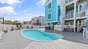 A pool area with a wooden deck, lounge chairs, and a multi-story building with balconies.