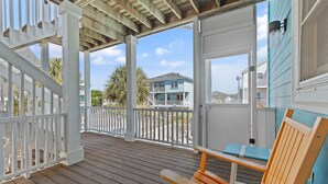A covered porch with a wooden bench, white railings, and a view of a blue house.