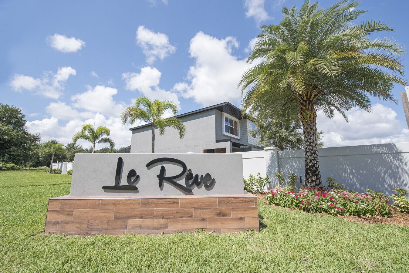 A sign with "Le Rêve" in front of a modern building with a grassy area and palm trees.