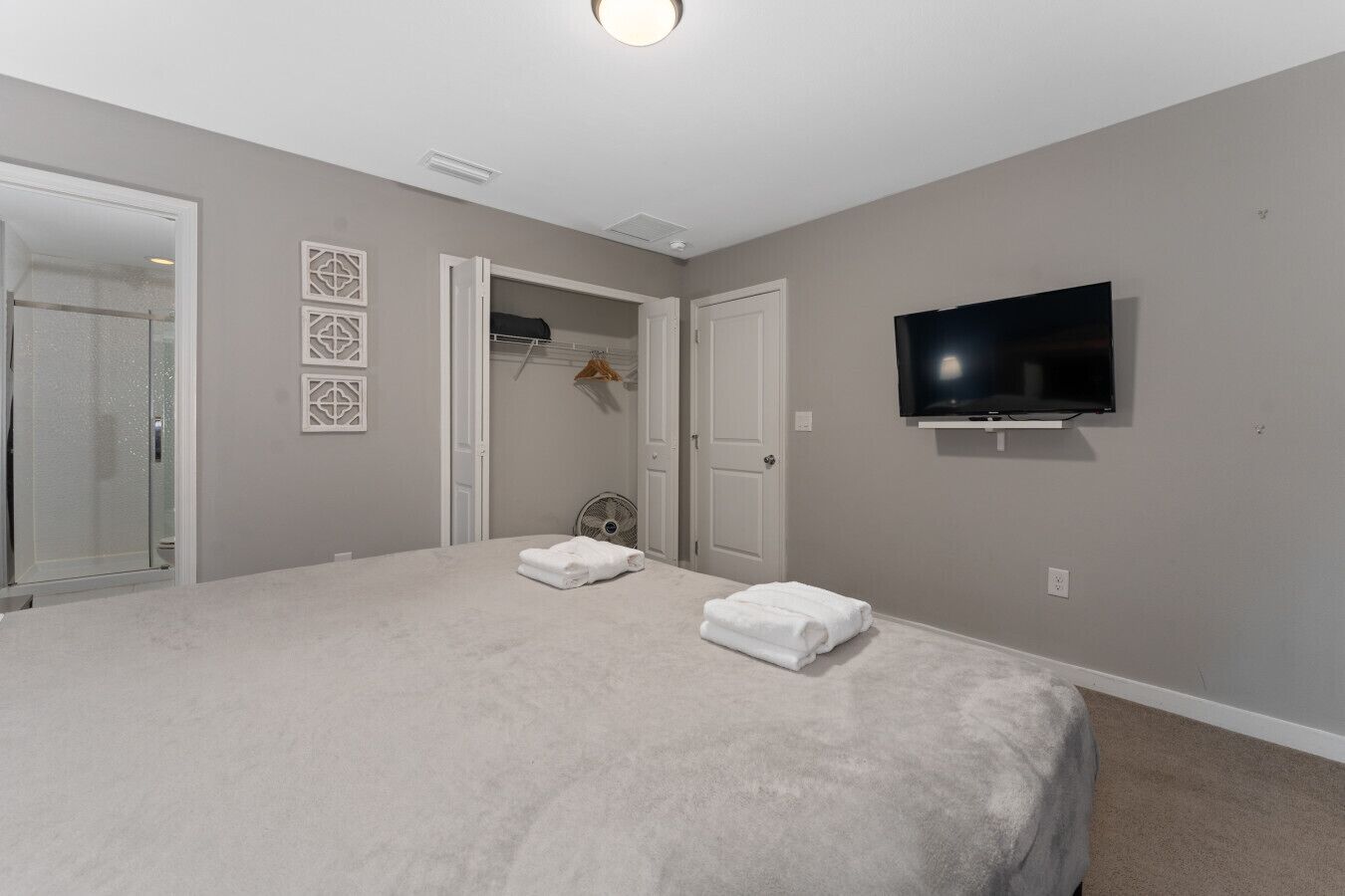 A bedroom with a large bed, a TV mounted on the wall, and a walk-in closet.