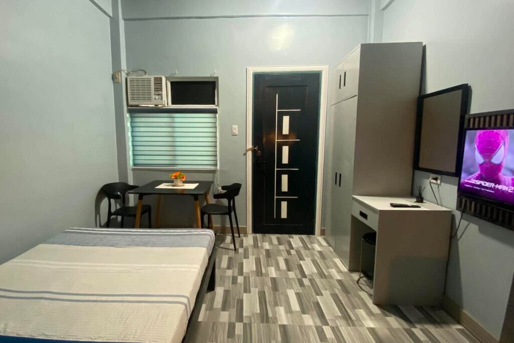Una habitación pequeña con cama, escritorio, silla, armario y televisión.