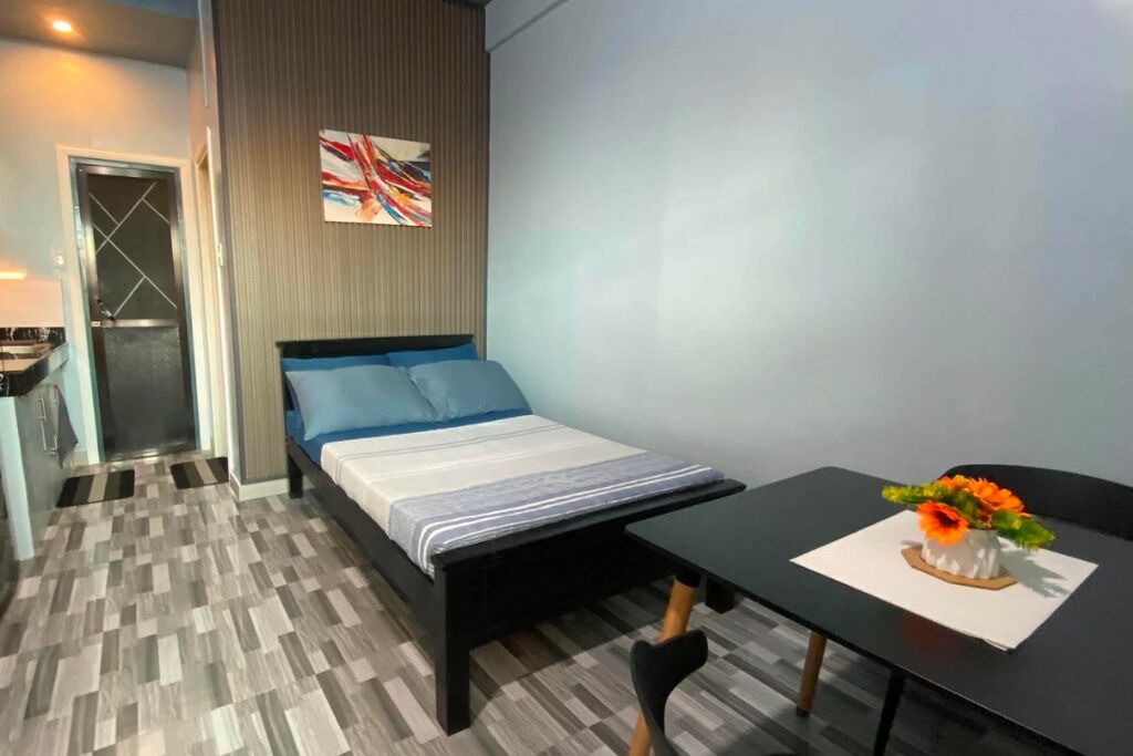 A modern bedroom with a bed, bedside table, and a small dining table with a vase of flowers.