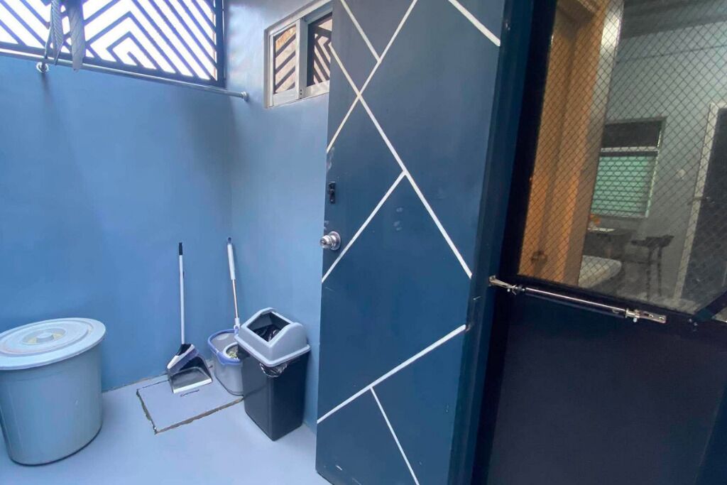 Un baño con una pared azul, un bote de basura blanco, un trapeador y un cubo.
