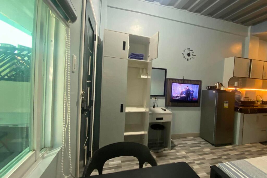 Una cocina compacta con refrigerador, una pequeña encimera y un televisor montado en la pared.