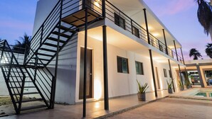 Un edificio moderno de dos pisos con una escalera a la izquierda, ventanas amplias y un área de piscina a la derecha.
