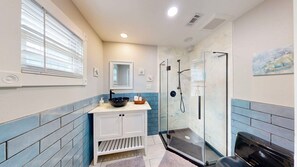 A modern bathroom with a glass shower enclosure, a white vanity with a black bowl sink, and a blue-tiled wall. - Pet Friendly, Old Town Location, Golf Cart Access, Close to the Beach (Port Aransas)
