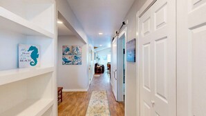 A hallway with white walls, wooden flooring, and a rug. There are shelves with artwork and a door on the right. - Pet Friendly, Old Town Location, Golf Cart Access, Close to the Beach (Port Aransas)