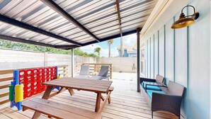 A covered outdoor area with a wooden table and chairs, a red and blue play structure, and a wall-mounted light fixture. - Pet Friendly, Old Town Location, Golf Cart Access, Close to the Beach (Port Aransas)