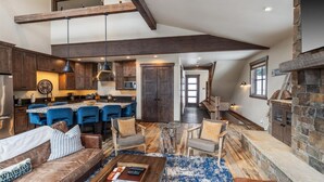 Un vaste espace de vie doté d’un haut plafond, une cuisine avec des meubles en bois foncé, un coin repas avec des chaises bleues et une cheminée en pierre.