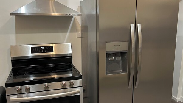 A kitchen with a stainless steel range hood, a built-in oven, and a refrigerator.