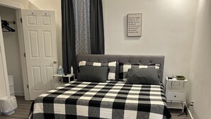 A neatly arranged bedroom with a checkered bedspread, a bedside table with a lamp, and a wall-mounted picture.