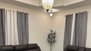 A living room with two dark leather sofas, a patterned rug, a tall plant, and a chandelier.