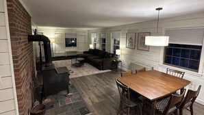 A spacious living area with a fireplace, a dining table with chairs, a sofa, and a large window.