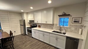 A modern kitchen with white cabinets, stainless steel appliances, and a wooden dining table.
