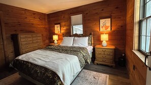 A wooden-paneled bedroom with a bed, two bedside tables with lamps, a dresser, and a window.
