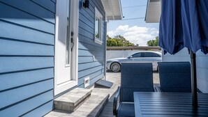 Et blå hus med en overdækket terrasse, en bil parkeret udenfor og et bord med stole.