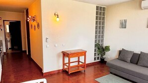 A living room with a sofa, a small wooden table, and a white chair. There is a tiled floor and a doorway leading to another room. - Torre Verde 2 Pools Tenis Praia da Rocha Beach (Portimão)