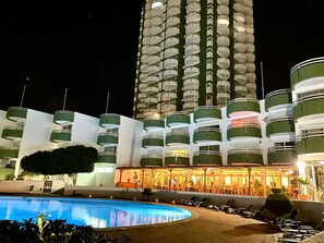 A hotel with multiple balconies, a swimming pool, and a well-lit lobby area.