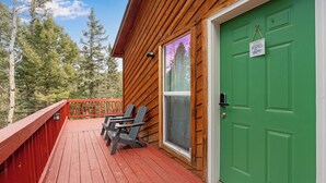 A wooden deck with two Adirondack chairs, a green door, and a window with a view of trees.