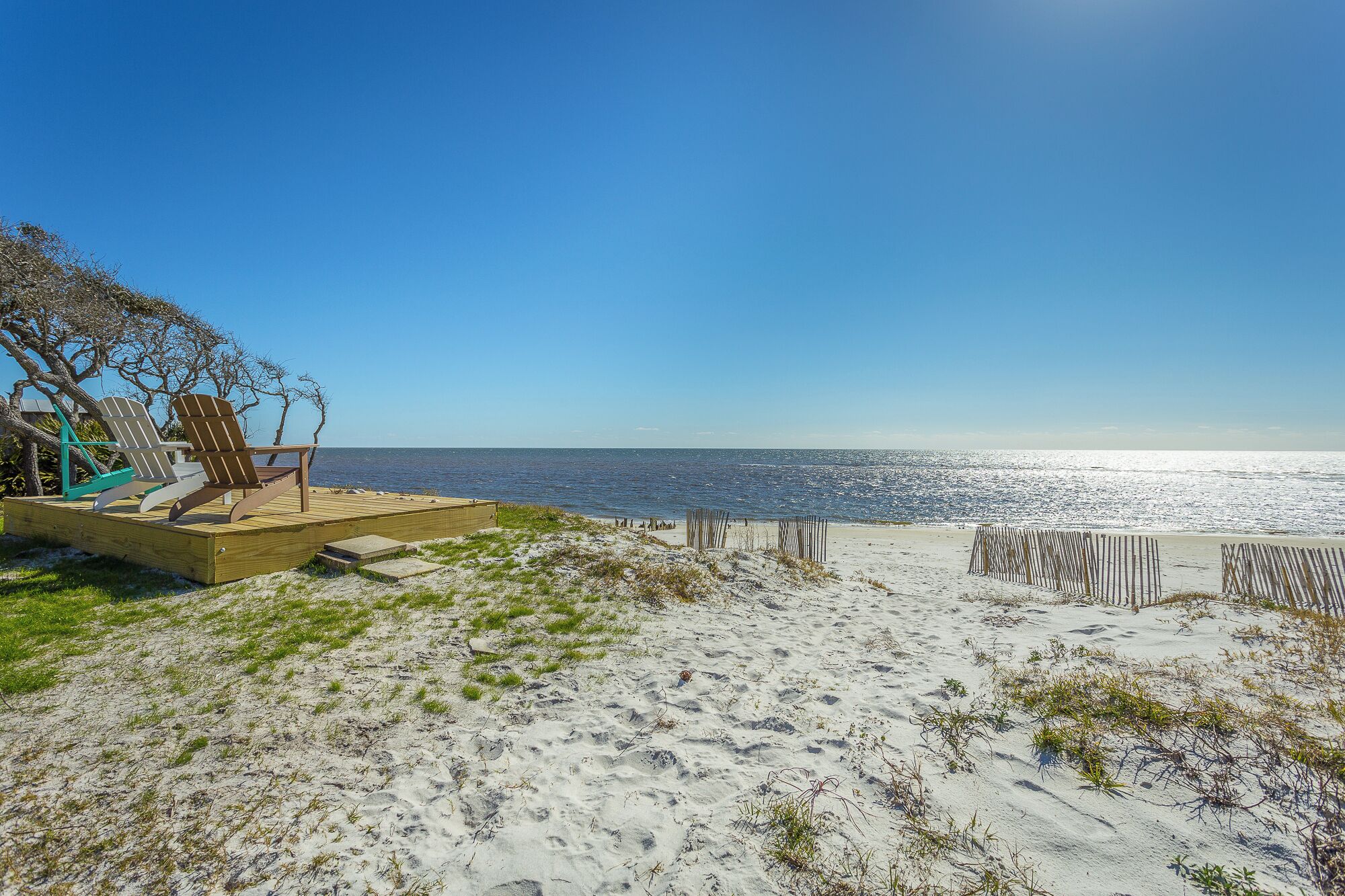 A beach with a wooden deck, beach chairs, and a view of the ocean.