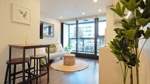 Una sala de estar moderna con un sofá, una mesa de comedor con sillas, un ventanal grande y una planta en maceta.
