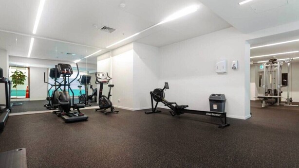 Un gimnasio con máquinas de cardio, una máquina de escaleras y un espejo grande.