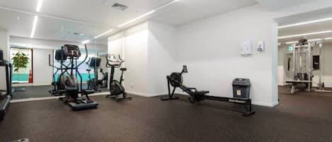 Un gimnasio con máquinas de cardio, una máquina de escaleras y un espejo grande.