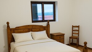 A wooden bed with a headboard, a bedside table, and a chair in a room with a window and tiled floor. - Casa Ref gio do Douro (Baiao)