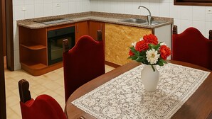 A modern kitchen with wooden cabinets, a granite countertop, and a built-in oven. There is a dining area with a table, chairs, and a vase of flowers. - Casa Ref gio do Douro (Baiao)