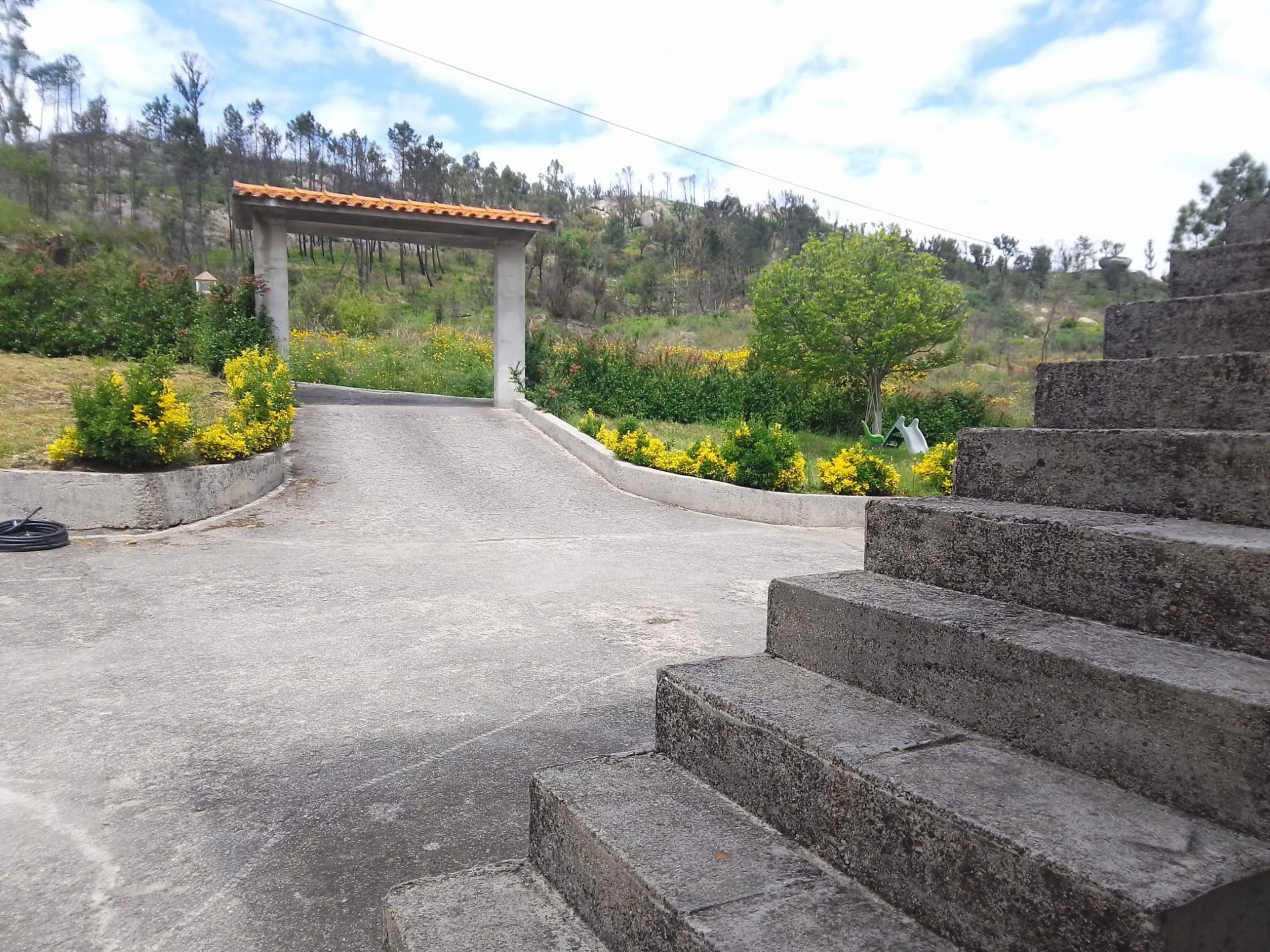 A concrete staircase leading up to a stone structure with a tiled roof, surrounded by greenery and a hilly landscape.