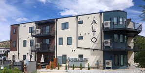 A modern multi-story building with balconies, outdoor seating, and a clear sky.