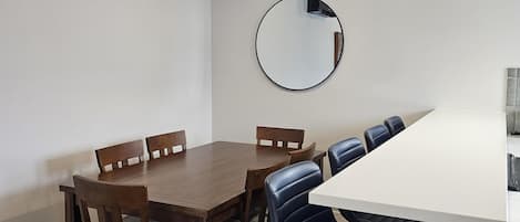 A dining area with a wooden table and chairs, a round mirror on the wall, and a black pendant light.