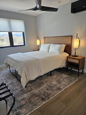 A bedroom with a bed, nightstands, a floor lamp, a ceiling fan, and a window with a view of mountains.