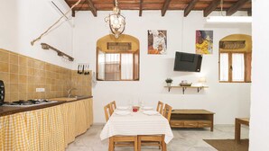 Una cocina con salpicadero de azulejos, armarios de madera, una mesa de comedor preparada para cuatro personas y un televisor montado en la pared.