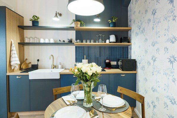Een moderne keuken met blauwe kastjes, een houten aanrecht en een eethoek met een ronde tafel voor twee personen.