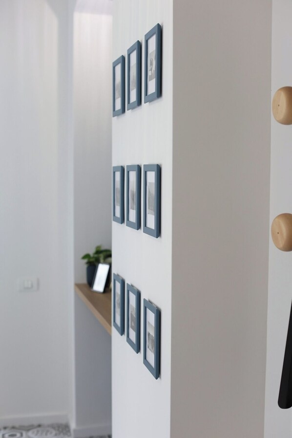 Un couloir avec des tableaux encadrés accrochés au mur, une étagère en bois ornée d’une plante et une porte dotée d’une poignée ronde.