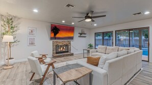 A modern living room with a fireplace, white sofas, a coffee table, and a large window overlooking a pool.