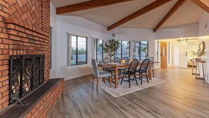 A dining area with a brick fireplace, wooden beams, and large windows.