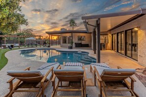 A modern outdoor pool area with lounge chairs and a covered patio.