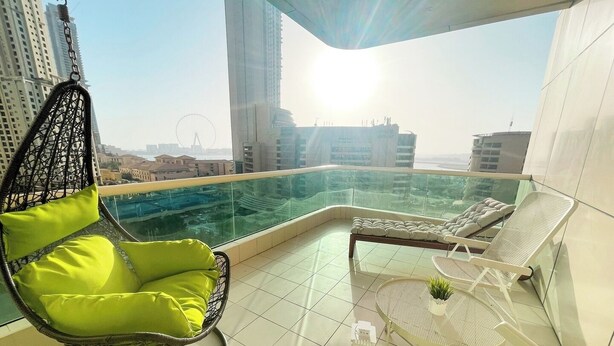 A balcony with a hanging chair, a sofa, and a small table with a plant.