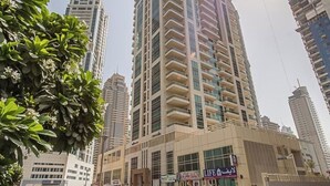 A tall, modern high-rise building with a glass facade, surrounded by other high-rise buildings and a well-maintained grassy area.
