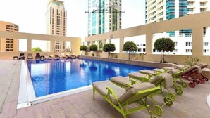 A rooftop swimming pool with lounge chairs and a view of high-rise buildings.