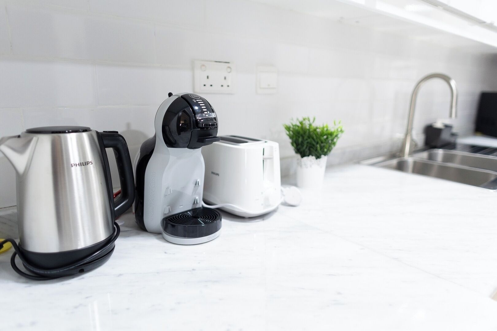 Una cucina con un bollitore in acciaio inossidabile, una macchina da caffè e un tostapane su un piano di lavoro bianco.