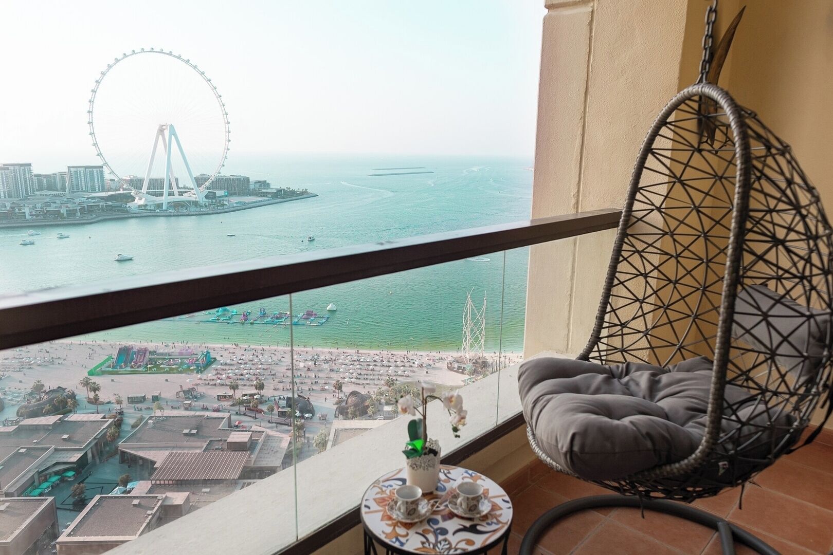 Ein Balkon mit einer Hängematte, einem kleinen Tisch mit Teekanne und Blick auf Strand und Riesenrad.