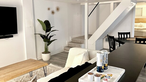 A modern living room with a flat-screen TV, a dining table with chairs, a potted plant, and a staircase leading to another level. - Chic Basement Suite ATL - Private Entrance & Free Charge and Park (Atlanta)
