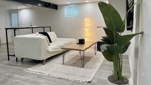A modern living room with a white sofa, a wooden coffee table, and a large green plant. - Chic Basement Suite ATL - Private Entrance & Free Charge and Park (Atlanta)